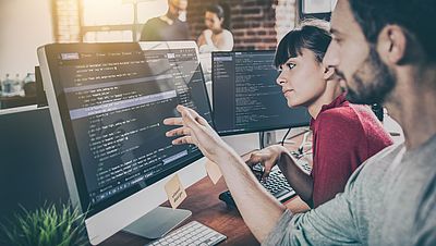 Junger Programmierer zeigt seiner Kollegin etwas auf dem Bildschirm